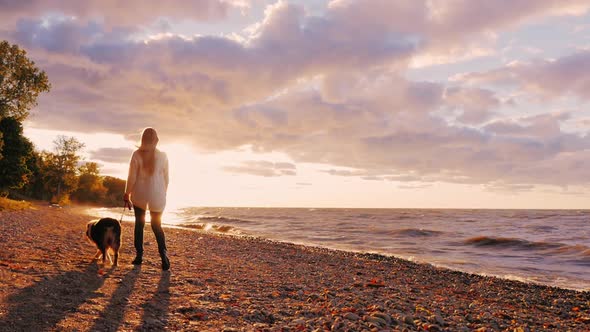 A Young Woman Walks Her Dog By the Lake at Sunset