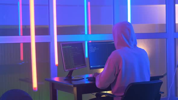 Back View of Hacker in White Hoodie Penetrating Network System in Neon Room