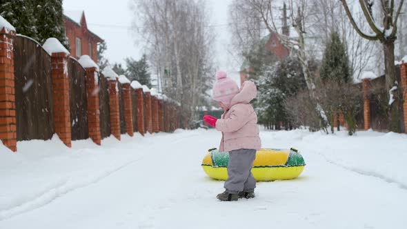 A small child tries to pull an inflatable circle on a rope on a snowy winter day