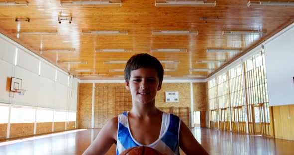 Portrait of schoolboy holding basketball in basketball court