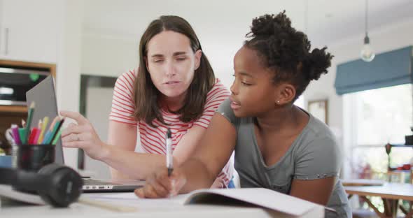 Happy caucasian woman and her african american daughter doing homework together