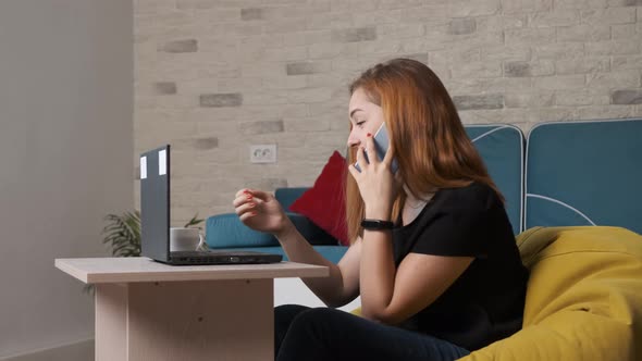 Woman Sits on the Couch, Talking on the Phone and Drinking a Cup of Coffee.