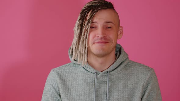 Young handsome man with blonde dreadlocks looking at camera, smiling on pink background.