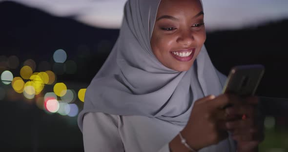 Muslim Woman Texting on Smartphone with Bokeh City Light in Background