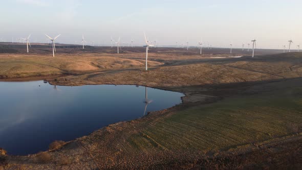 Wind turbine reflecting over lake waters, Scotland. Aerial forward