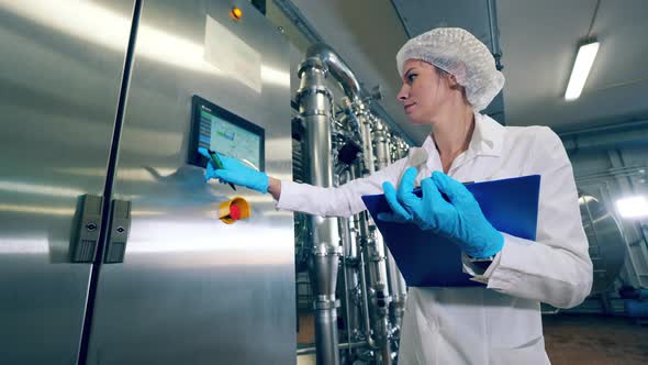 Plant Worker Checks a Machine, Typing on Display. Female Worker Controls the Quality of Production