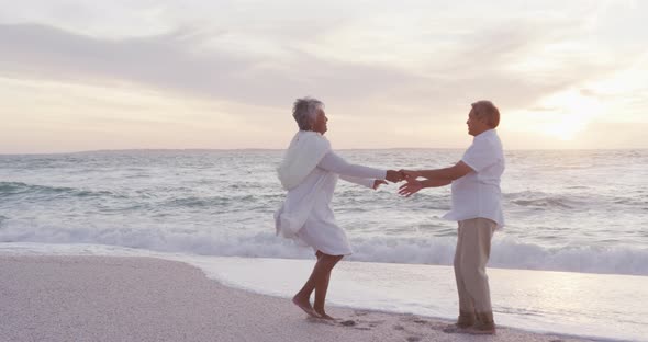 Happy hispanic just married senior couple dancing on beach at sunset