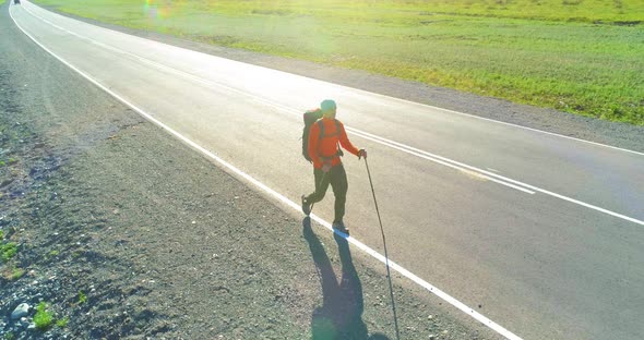 Flight Over Hitchhiker Tourist Walking on Asphalt Road. Huge Rural Valley at Summer Day. Backpack