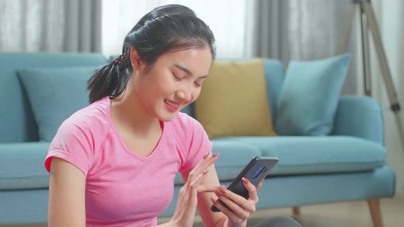 Asian Female Fitness Girl Is Using An App On Her Smartphone Before Working Out In Living Room