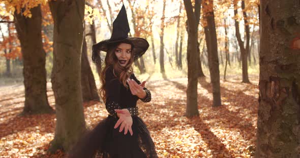 Attractive Woman in a Special Dress and Hat Looks Like a Witch in the Autumn Forest