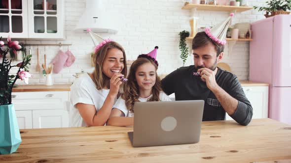 Happy Family with a Daughter Sitting in Kitchen and Celebrating Birthday Using Laptop for a Video