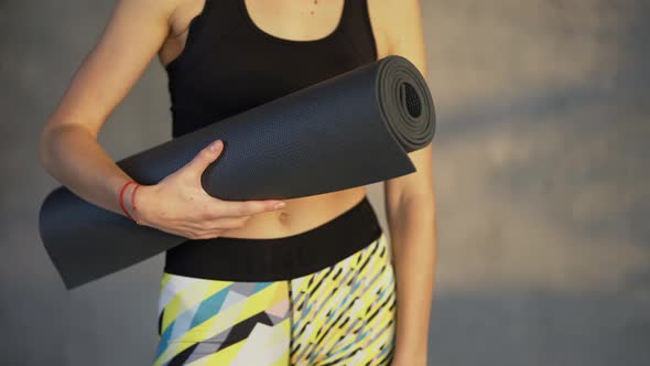 Close Up Overview of a Woman Athlete Posing with Mat in Hand Standing in Loft Room