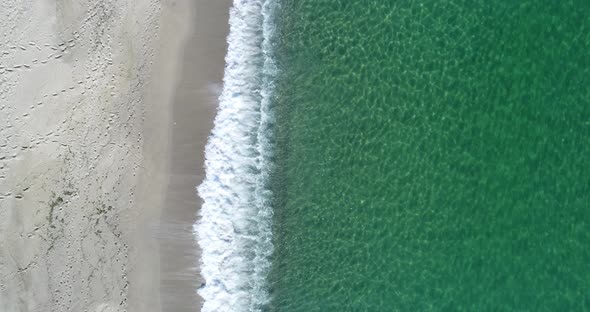 Static top down view of tropical beach, foamy ocean waves washing sand. Waves hitting sand beach