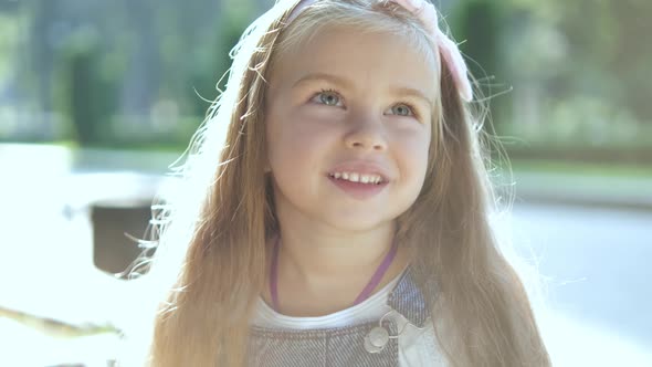 Portrait of pretty child girl standing outdoors in summer park smiling happily.