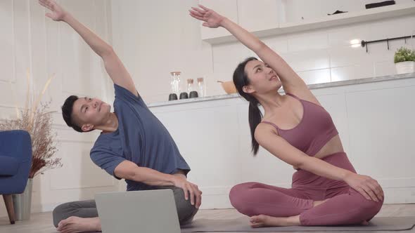 Asian sporty couple watching video tutorial practice yoga lesson at home