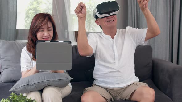 Asian elderly couple using tablet and virtual reality simulator playing games in living room.