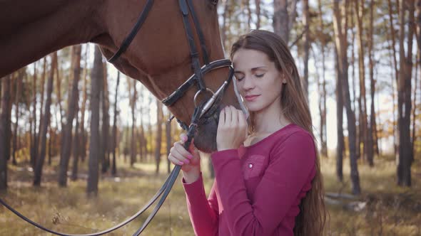 Close-up of a Young Caucasian Girl in Pink Clothes Caressing Horse in the Autumn Forest and Smiling