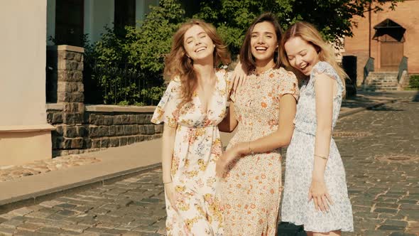 Three young beautiful girls posing outdoors at summer sunny day