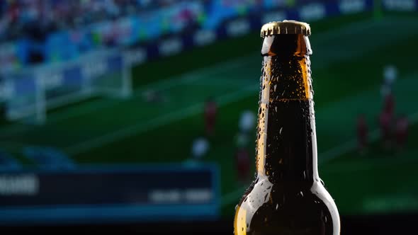 Glass Bottle of Beer Spinning Against the Background of the Broadcast of the Football Championship