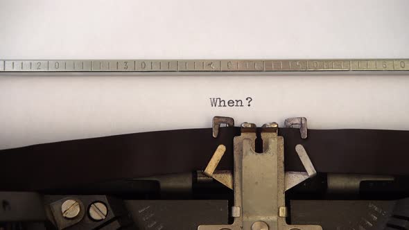 Typing word When ? on retro typewriter. Close up.