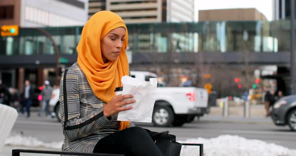 Side view of young Asian woman in hijab eating food in the city 4k