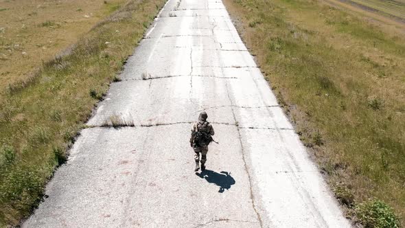 Back View of a Lone Tired Soldier Walks Along an Old Concrete Road