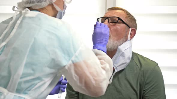 Lab Technician in a Protective Suit Takes a Swab From an Elderly Patient for Coronavirus