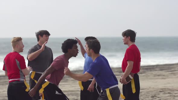 A group of guys playing flag football on the beach.