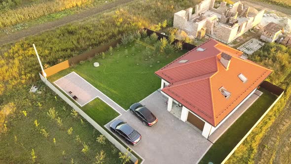 Top down aerial view of a private house with red tiled roof and spacious yard with parked two new 