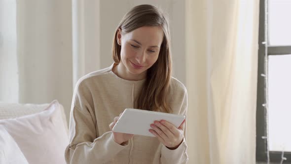 Young Woman Sits on the Bed and Using Digital Tablet