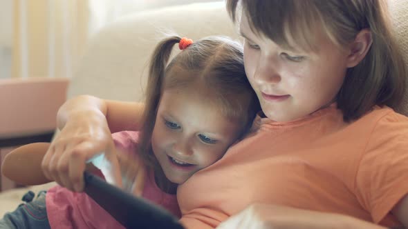 Two Girls Children Sister At Home On Couch Playing On Tablet