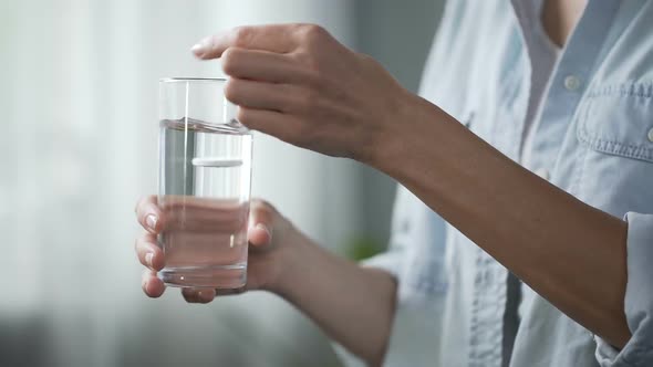 Woman taking painkillers, throwing aspiring into water glass, medication