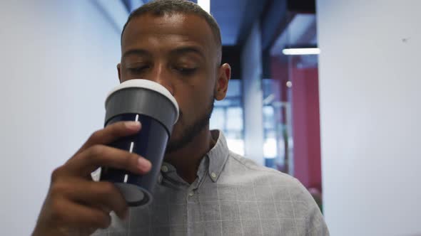 Mixed race businessman walking and drinking a cup of coffee in modern office
