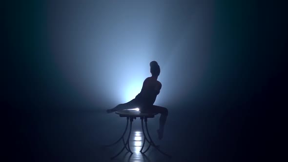 Speech Flexible Acrobat on the Table in the Studio. Smoke Background. Slow Motion. Silhouette