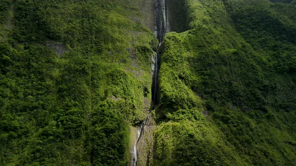 Aerial view of a waterfall on the side of a mountain on the Reunion Island. Sunlight break through t