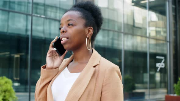 Positive Black Businesswoman Walking Outdoors and Chatting on Phone