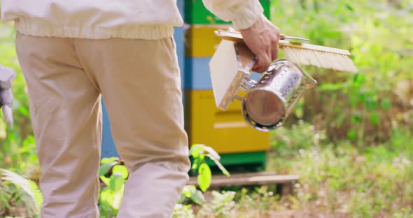 Beekeeper in White Protective Suit Goes Away From the Camera Towards the Hives in Background He