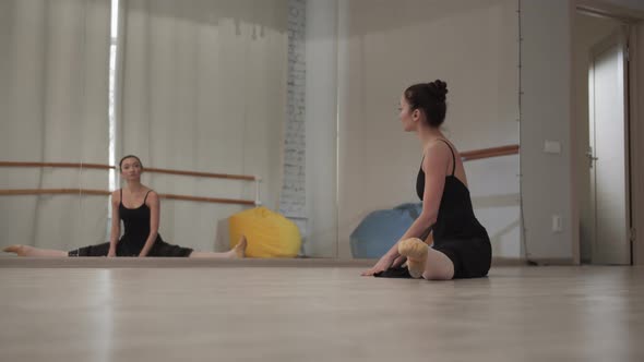 Before a Rehearsal in a Dance Hall, a Beautiful Ballerina Stretches Her Arms and Legs While Sitting