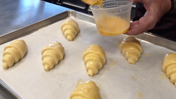 A Baker painting Egg wash on to croissants that will be baked in a cafe