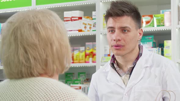 Handsome Young Pharmacist Handing Shopping Bag with Purchase To a Customer