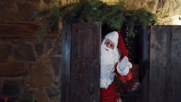Santa is waving his hand while standing at the door.