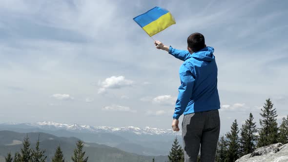 Man stands holding an Ukraine flag waving in slow motion at a bright overlook