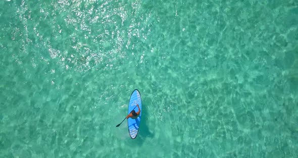 Aerial drone view of a man paddling an SUP stand-up paddleboard near a tropical island