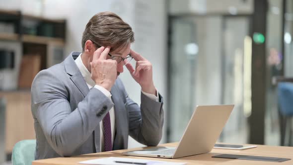 Stressed Businessman with Laptop Having Headache in Office