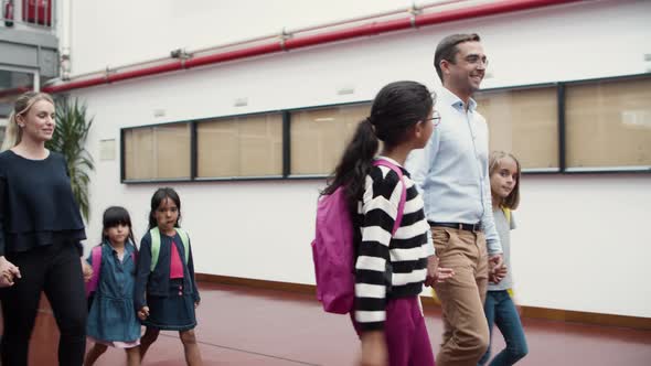 Male and Female Teachers Walking with Kids in School Corridor