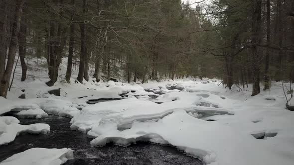 Drone flying low above snowy river in winter