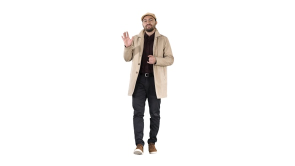 Young man in trench coat makes hi gesture on white background.