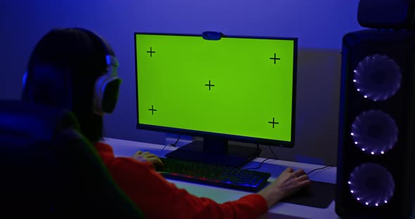 Gamer Sits at a Large Computer Monitor with a Green Screen
