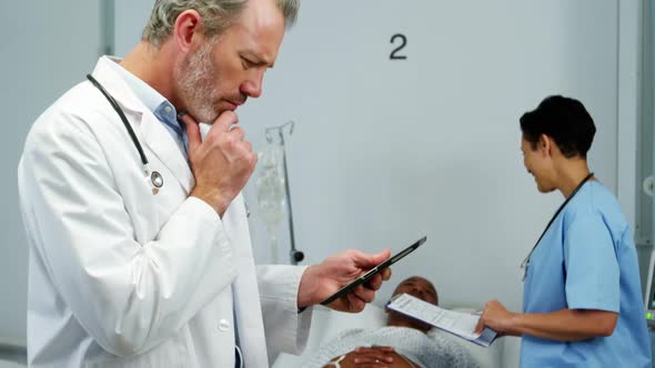 Doctor using digital tablet while nurse interacting with patient