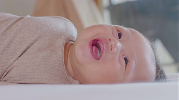 An Asian newborn baby is laying down on a soft white sheet mattress